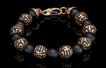 Black matte beaded bracelet with patterned rose gold metal beads and a rose gold lobster clasp on a reflective surface.