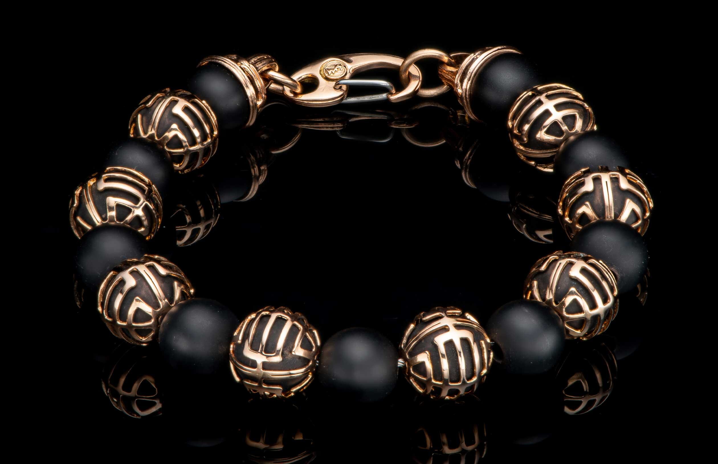 Black matte beaded bracelet with patterned rose gold metal beads and a rose gold lobster clasp on a reflective surface.