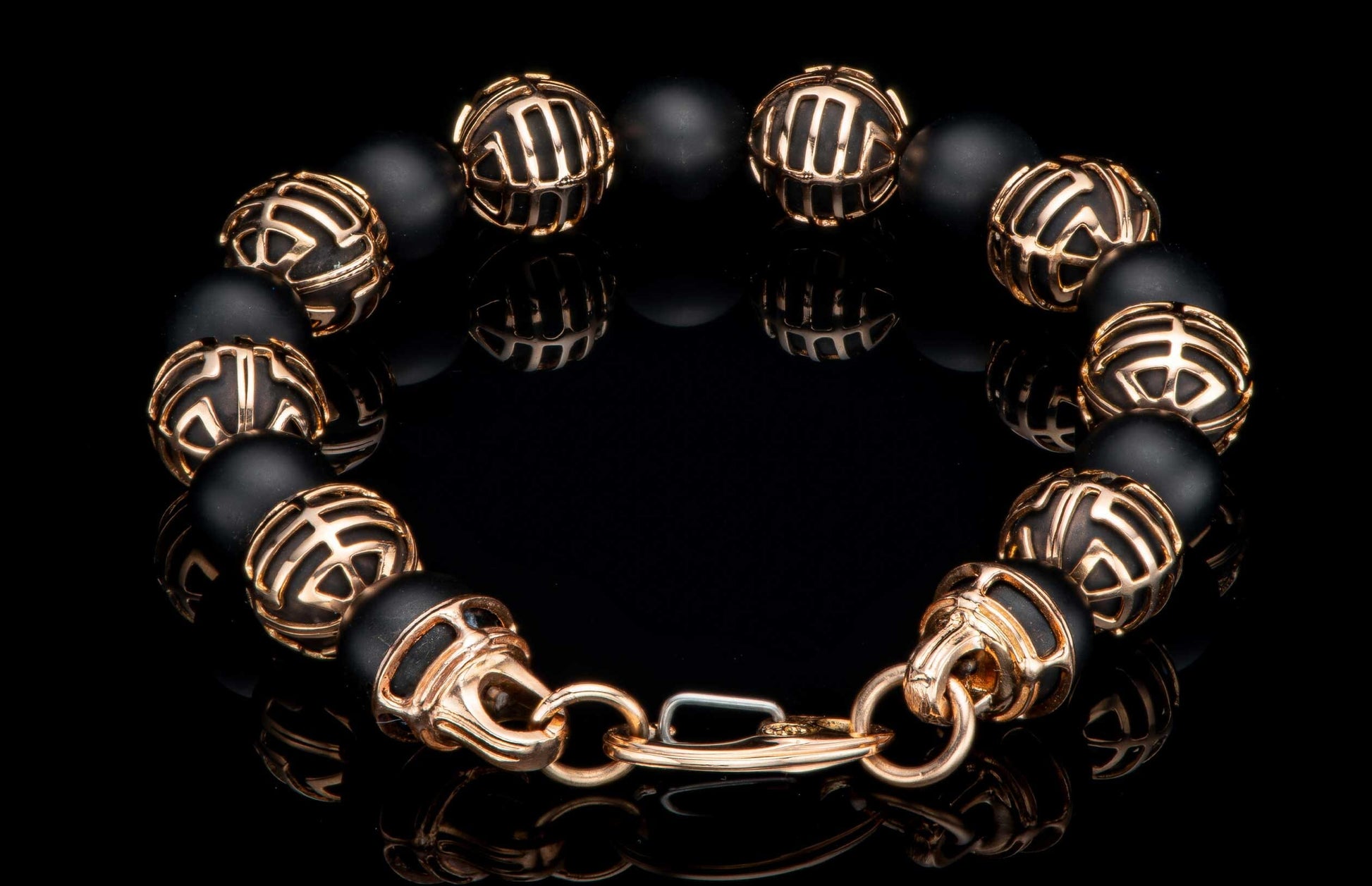 Black beaded bracelet with ornate gold-tone patterned spacers and clasp, reflecting on a dark surface.