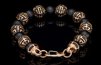Black beaded bracelet with ornate gold-tone patterned spacers and clasp, reflecting on a dark surface.