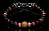 Beaded bracelet with dark red, black, and marbled beige stones, intricate gold-tone carved beads, and a silver chain clasp.