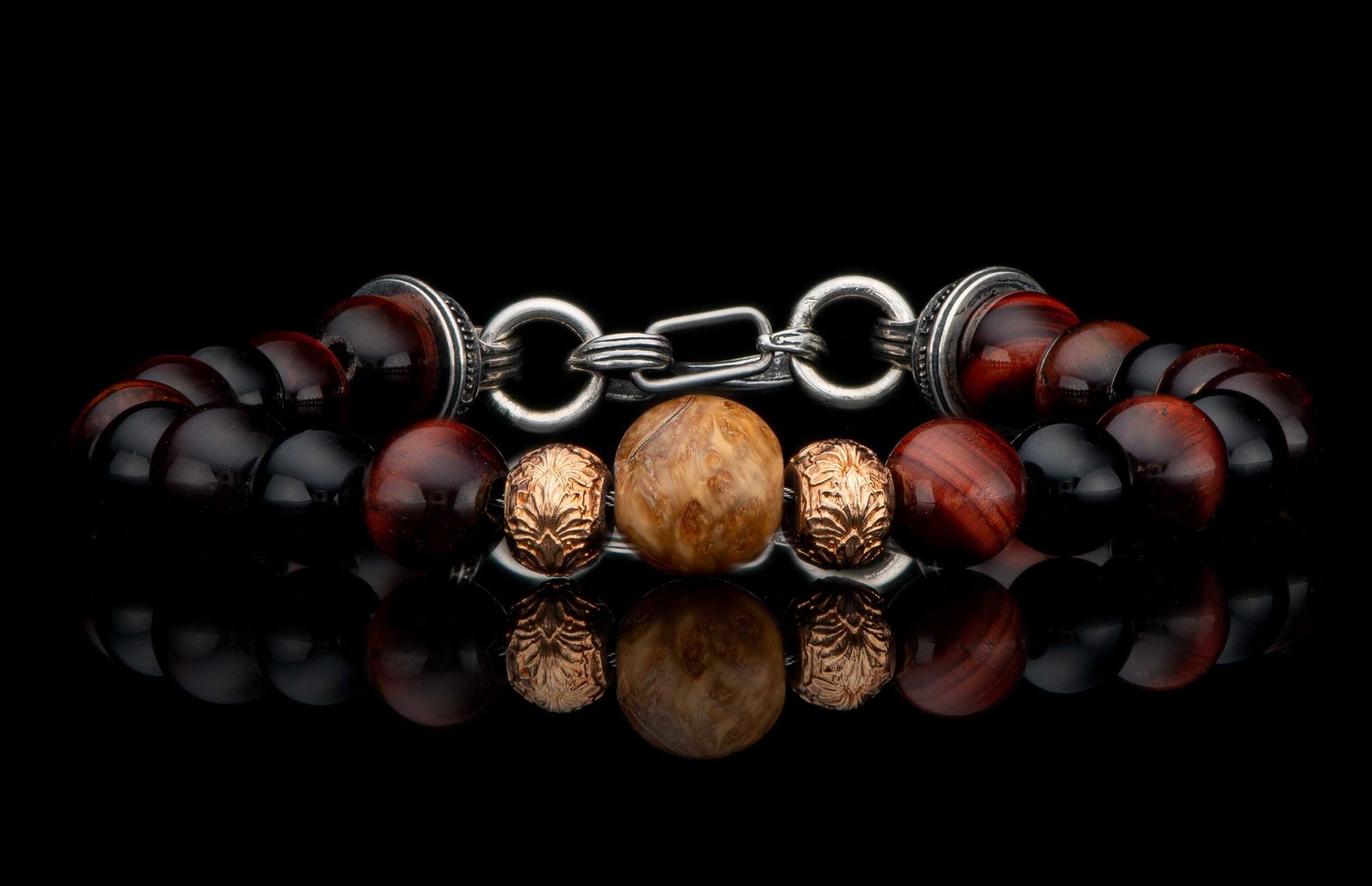 Beaded bracelet with dark red, black, and light brown textured beads, featuring ornate silver-tone metal rings and clasp, laid flat with reflection.