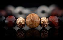 Beaded bracelet with dark red, golden brown, black, and bronze patterned beads reflecting on a dark surface.