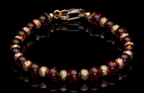 Beaded bracelet with reddish-brown amber-like beads, intricately patterned gold-toned spacers, and a lobster clasp on a reflective black surface.