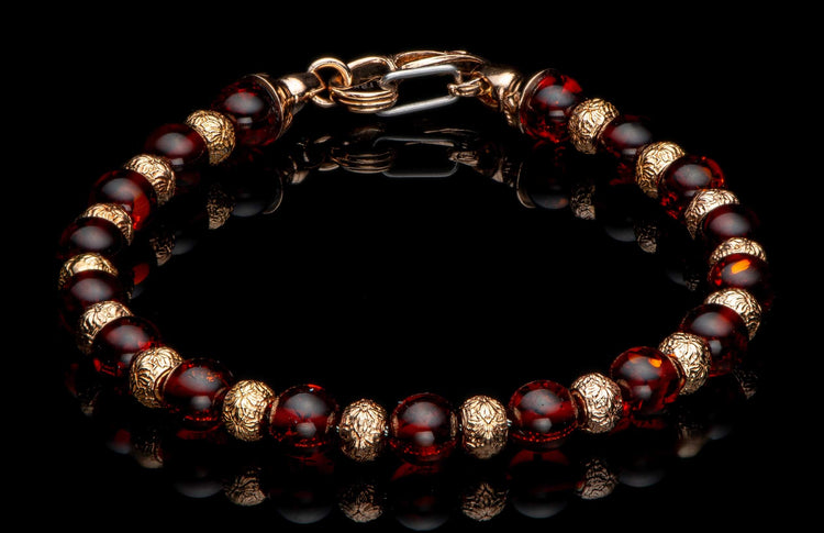 Beaded bracelet with reddish-brown amber-like beads, intricately patterned gold-toned spacers, and a lobster clasp on a reflective black surface.