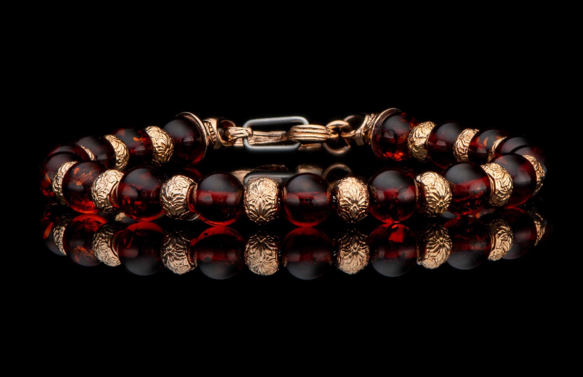 Dark amber bead bracelet with ornate gold-tone floral accents and clasp, reflecting on a polished black surface.