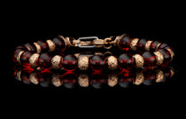 Dark amber bead bracelet with ornate gold-tone floral accents and clasp, reflecting on a polished black surface.