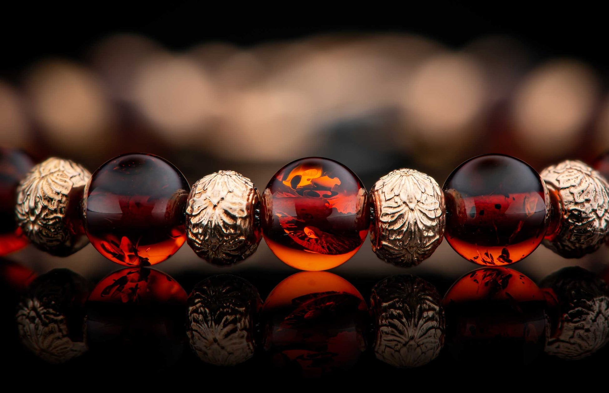 Jewelry bracelet with polished dark amber and intricately carved golden beads, reflecting on a black surface.