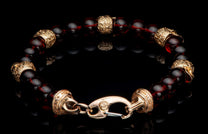 Dark red beaded bracelet with ornate gold-tone carved metal elements and a detailed hook clasp, reflecting on black.