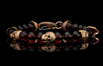 Dark amber beaded bracelet with gold skull charms and clasp, reflected on a black surface.