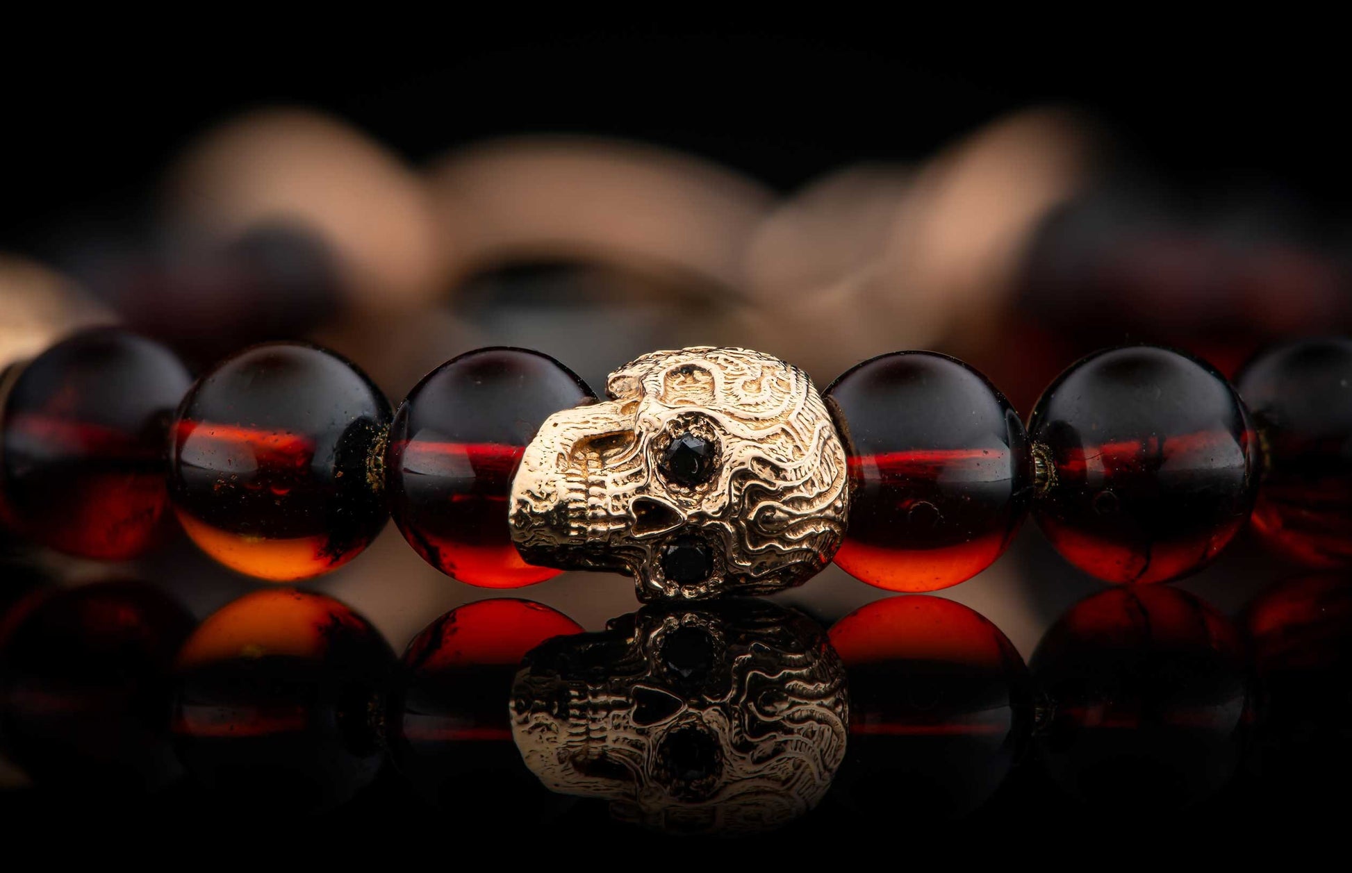 Beaded bracelet with dark amber beads and a textured gold skull charm featuring black stones.