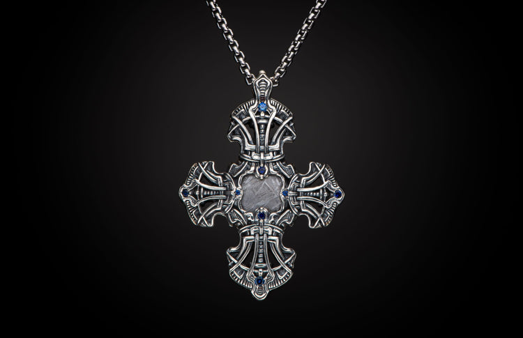 Intricately designed silver cross pendant featuring blue gemstones and a rectangular meteorite inlay with Widmanstätten pattern, on a silver chain.