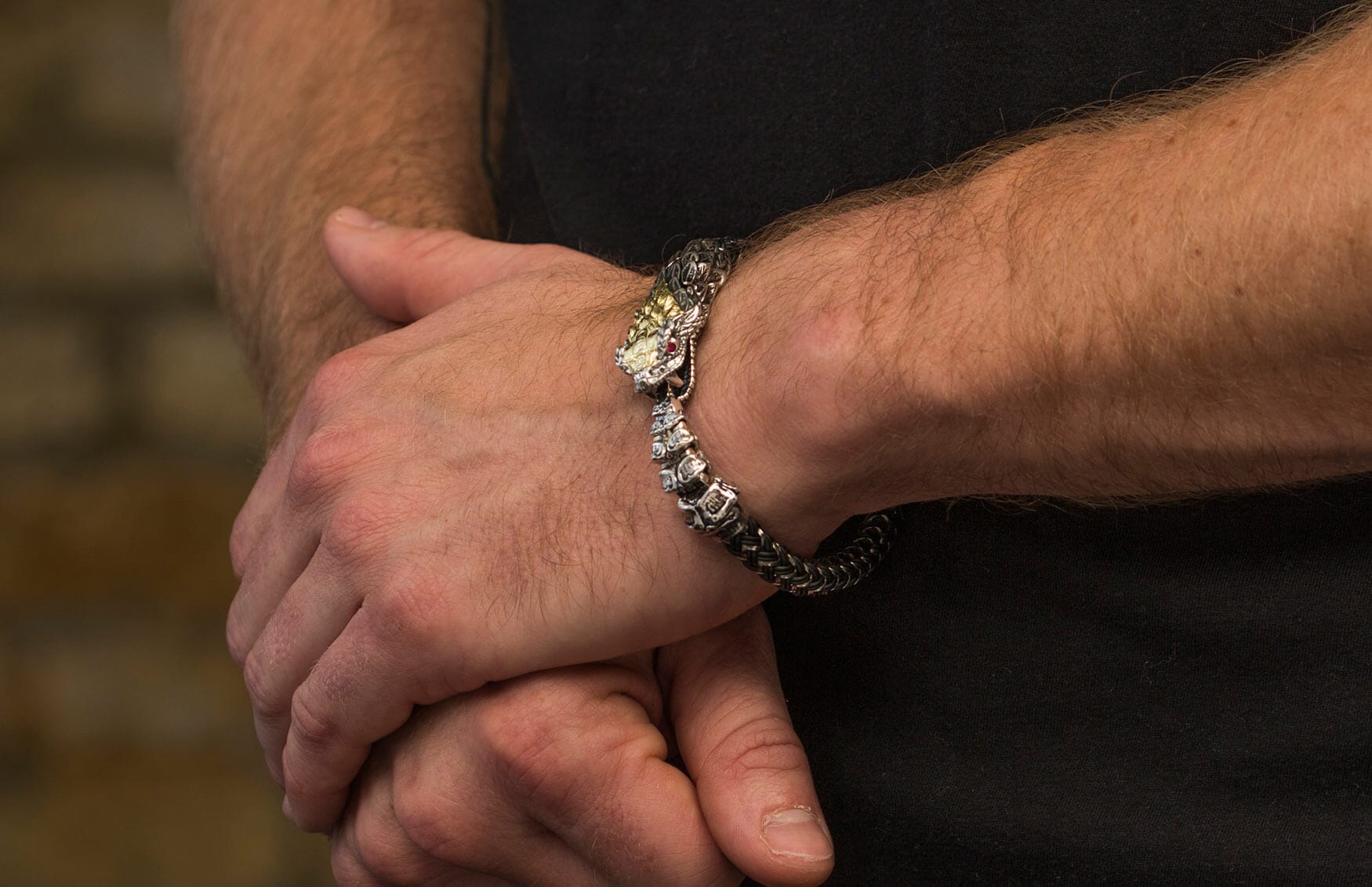 Snake-head bracelet with a textured silver-tone body and gold-tone head, featuring a red eye and white stone, worn on a man's arm.