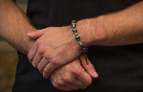 Textured lava bead and silver-toned spacer bracelet with black cord on a man's wrist.