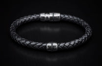 Black braided leather bracelet with a silver metal bead featuring a wavy pattern and a blurred magnetic clasp.