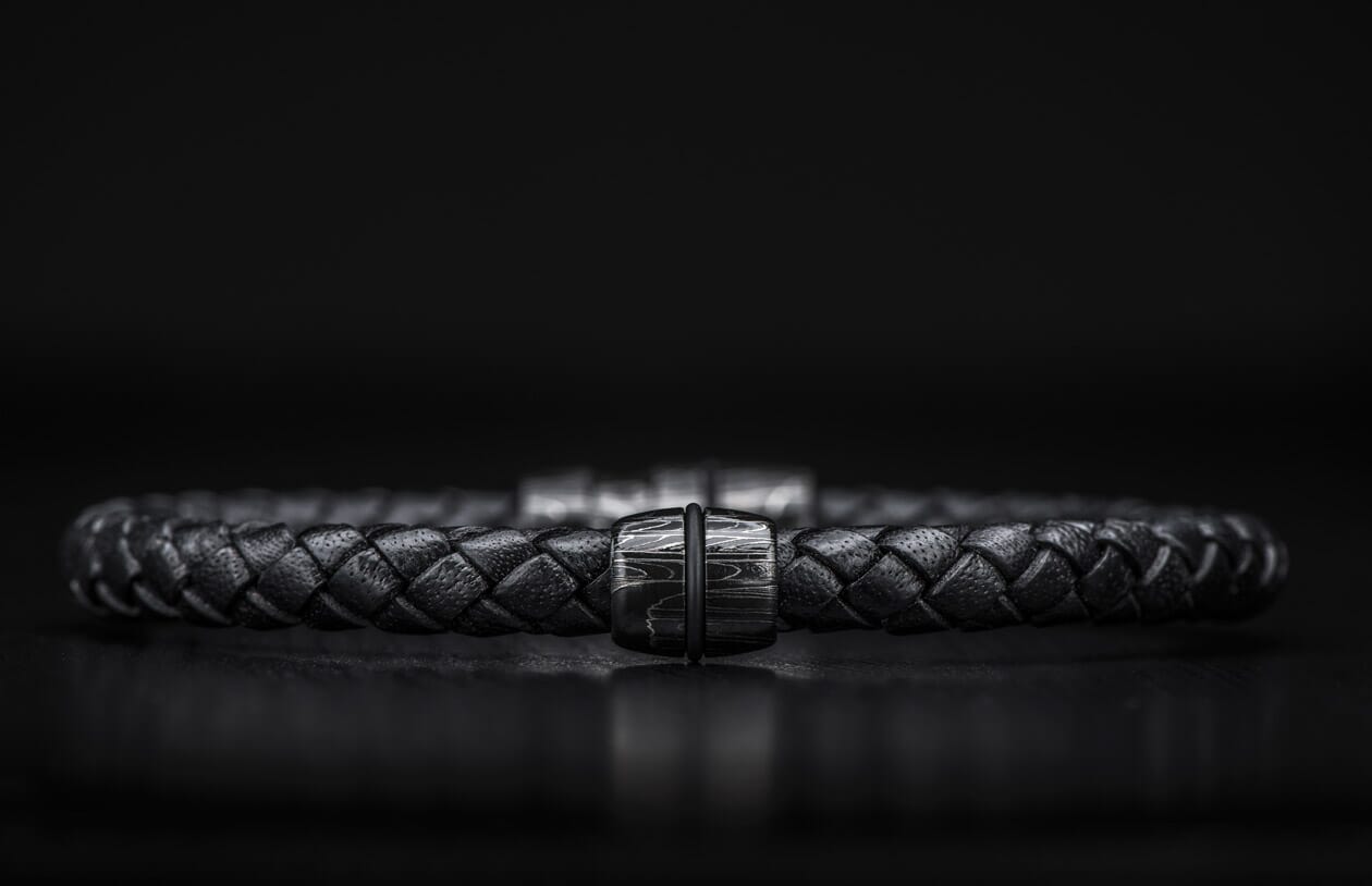 Black braided leather bracelet with a dark metal clasp featuring a distinct wavy pattern, centered.
