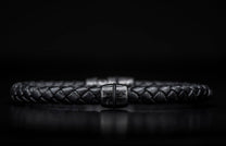 Black braided leather bracelet with a dark metal clasp featuring a distinct wavy pattern, centered.
