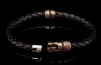 Black braided leather bracelet with mokume-gane patterned beads, black rubber rings, and an open clasp featuring an orange gemstone.
