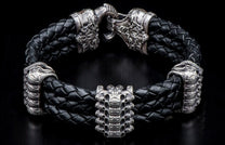Black braided leather bracelet with ornate antique silver lion head clasp and stacked skull centerpiece.