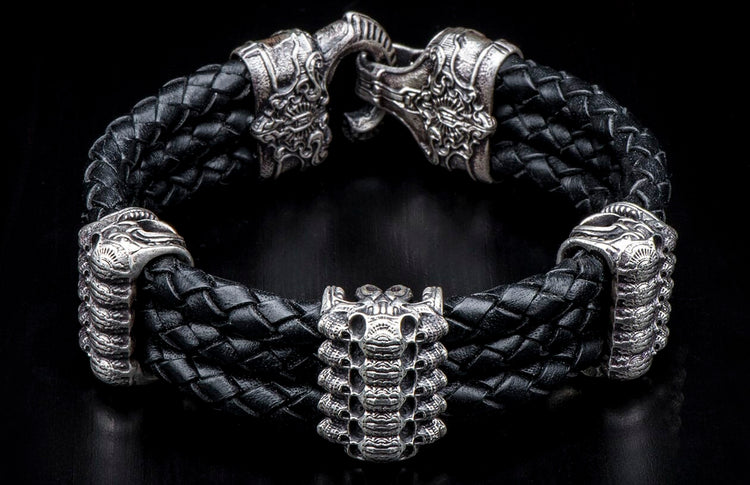 Black braided leather bracelet with ornate antique silver lion head clasp and stacked skull centerpiece.
