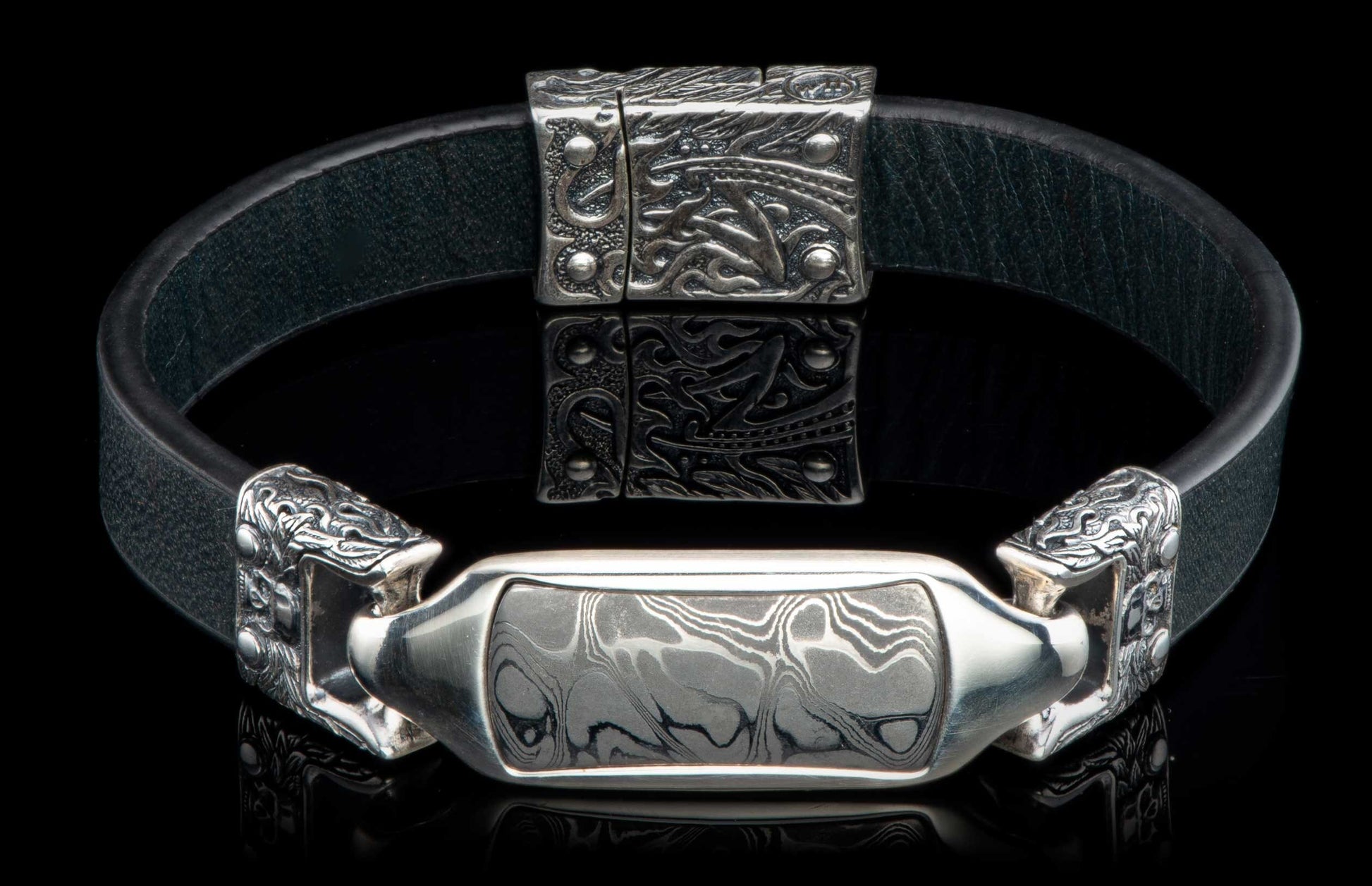 Black leather bracelet with an ornate silver centerpiece and Damascus steel inlay.