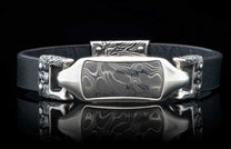 Black leather bracelet featuring a Damascus steel inlay framed by ornate silver-toned metalwork with skull details.