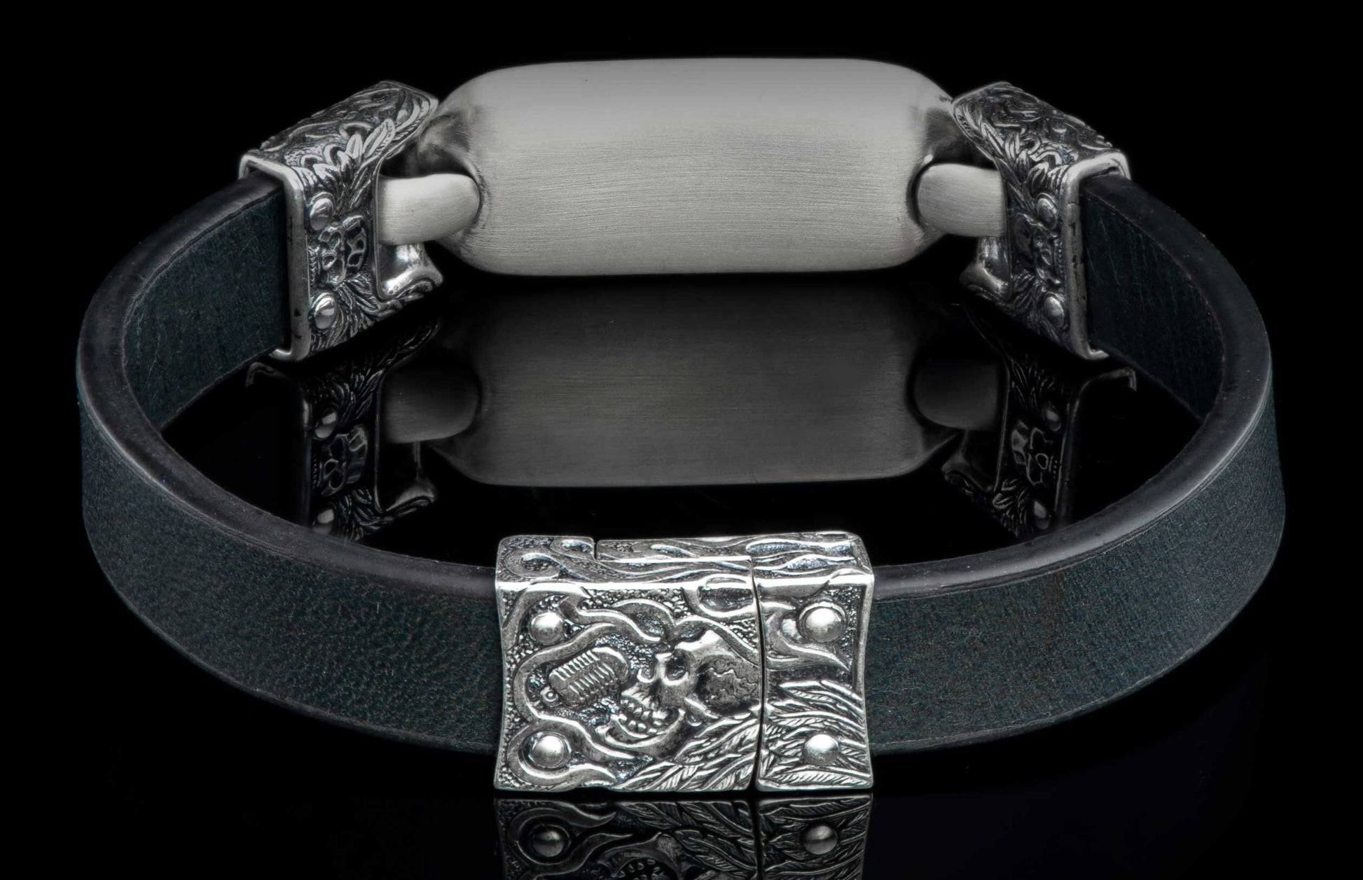 Black leather bracelet with a brushed silver metal plaque and ornate silver skull-motif clasp.