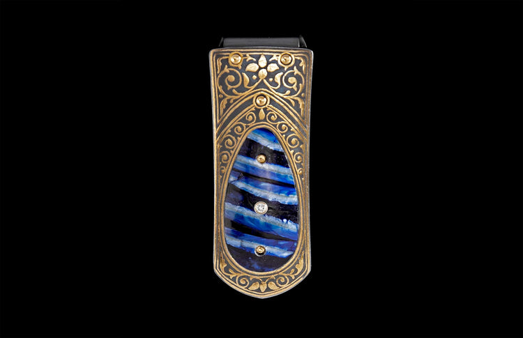Ornate money clip with gold-toned scrollwork and a central blue-striped inlay, accented with two diamonds and three gold studs.