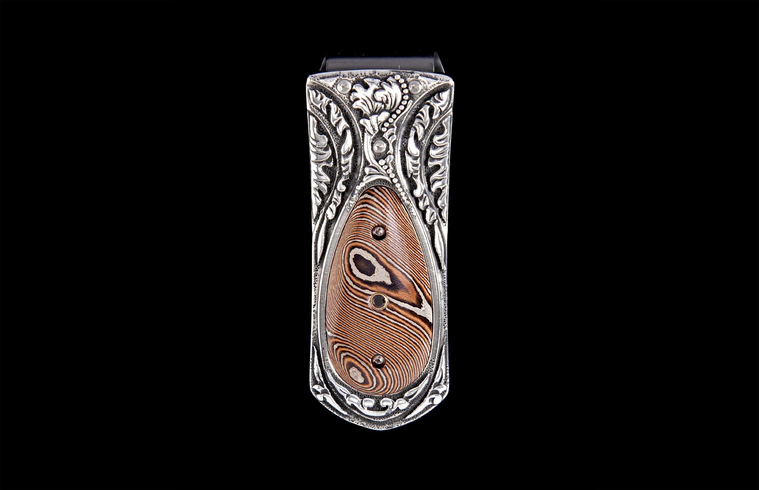 Money clip with ornate silver-toned engraved frame and a brown and silver striped inlay featuring black accents.