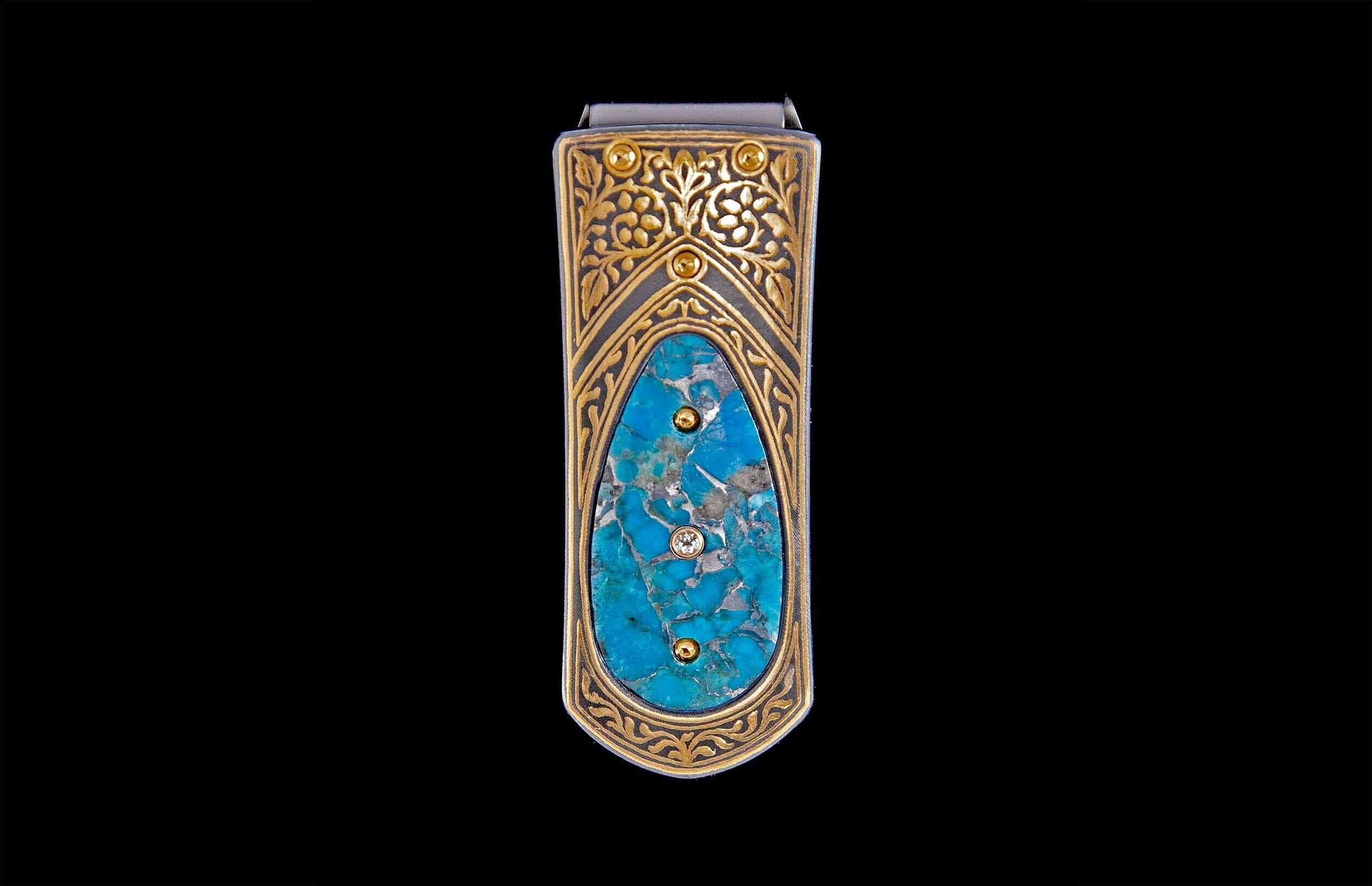 Ornate money clip featuring a central turquoise stone with a clear gemstone, framed by gold filigree and two gold studs.