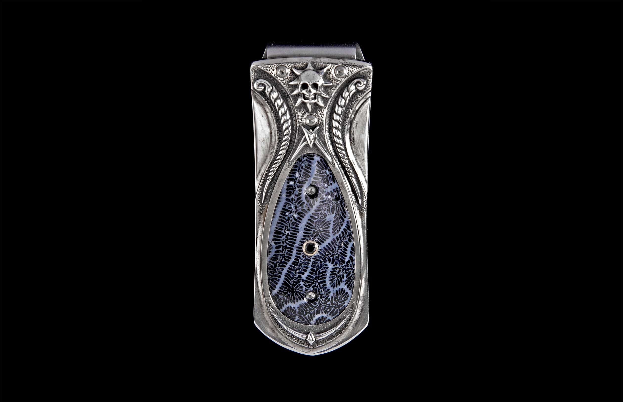 Silver-toned money clip with skull and sunburst, intricate scrollwork, and a dark blue fossilized coral inlay with small embedded accents.