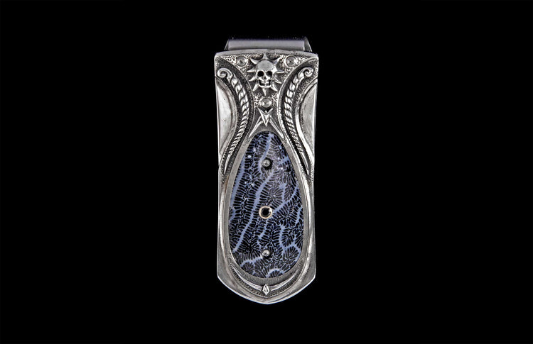 Silver-toned money clip with skull and sunburst, intricate scrollwork, and a dark blue fossilized coral inlay with small embedded accents.