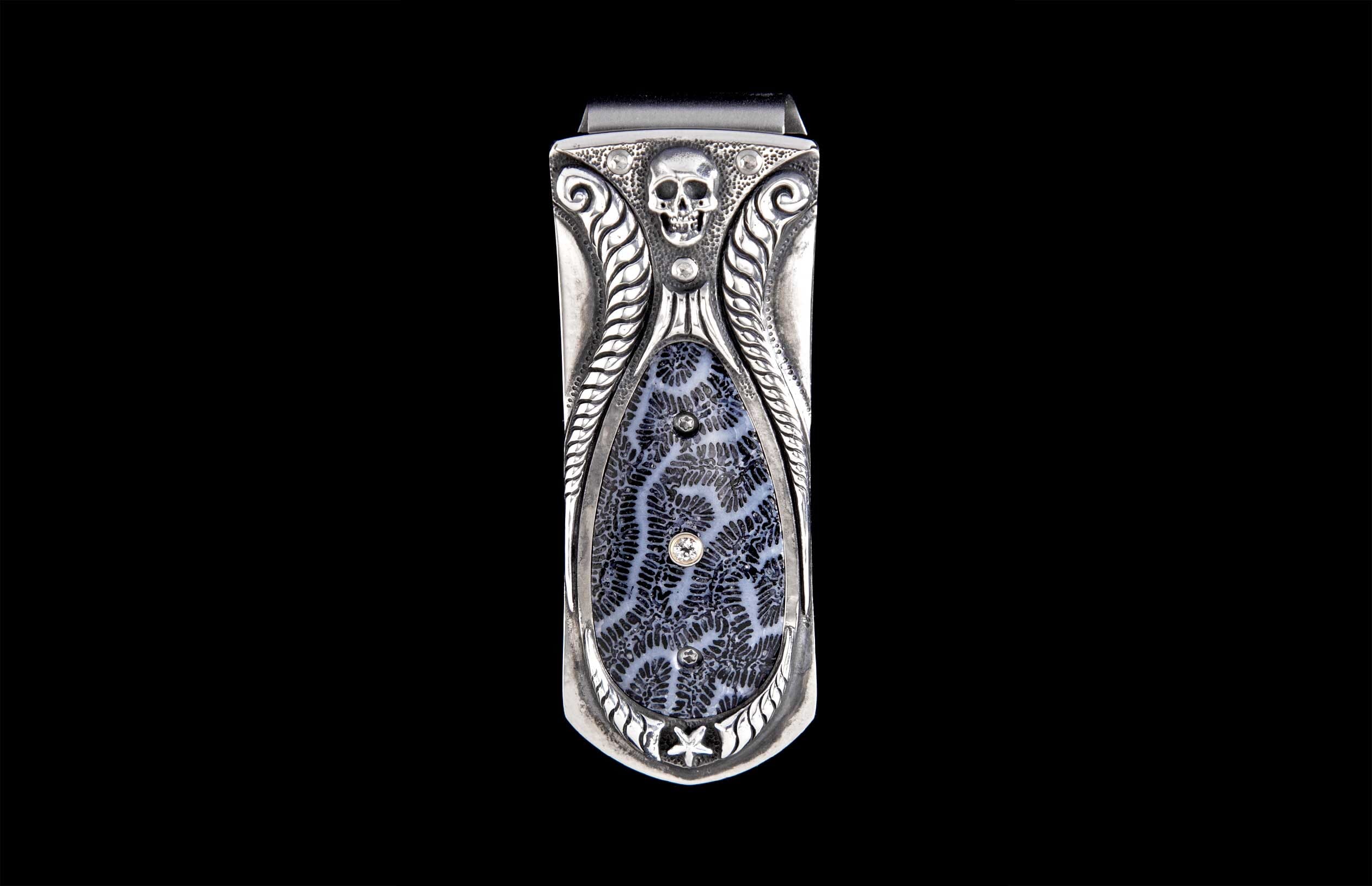 Ornate silver-toned money clip with a skull, leafy scrollwork, and a black-and-white fossilized coral inlay featuring clear gemstones and a star.
