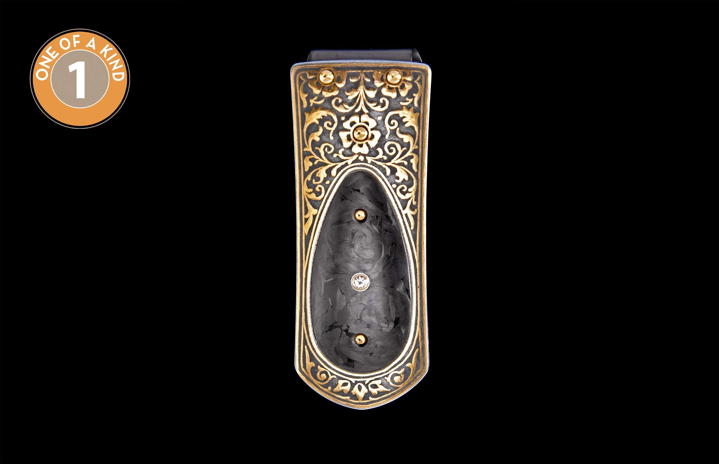 Ornate gold filigree money clip with a dark background and a central black insert featuring gold studs and a clear gemstone.