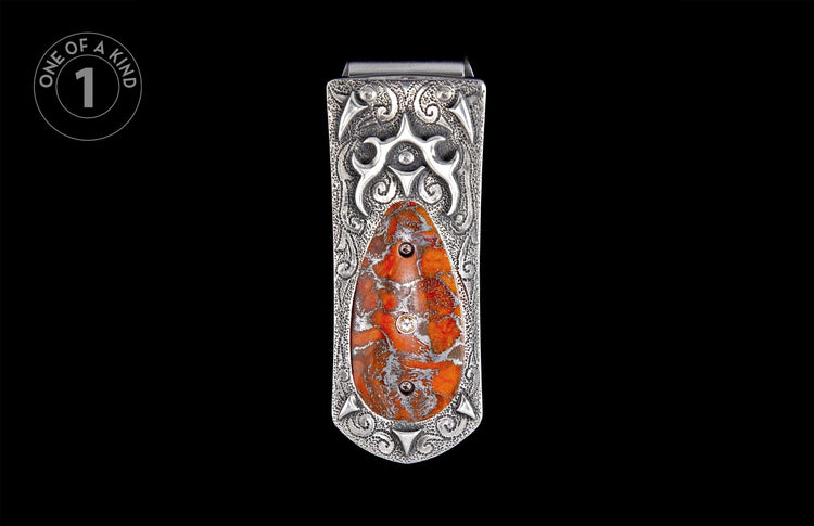 Ornate silver-toned metal money clip with intricate scrollwork, an oval orange-red patterned stone inlay, and three small round accents.