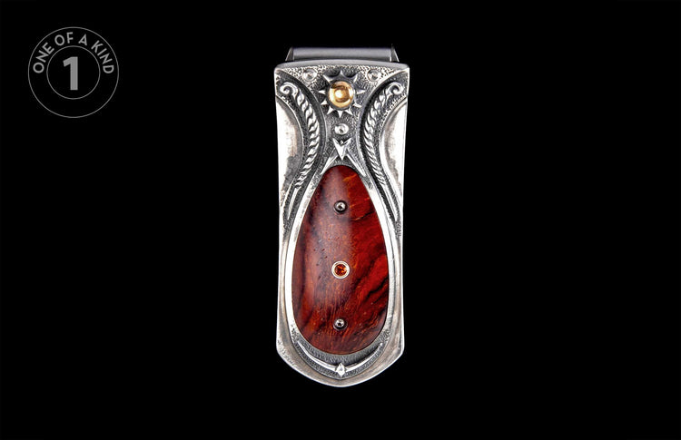 Ornate silver money clip featuring intricate engravings, a gold sunburst with a spherical accent, and a reddish-brown wood inlay with a red gemstone.