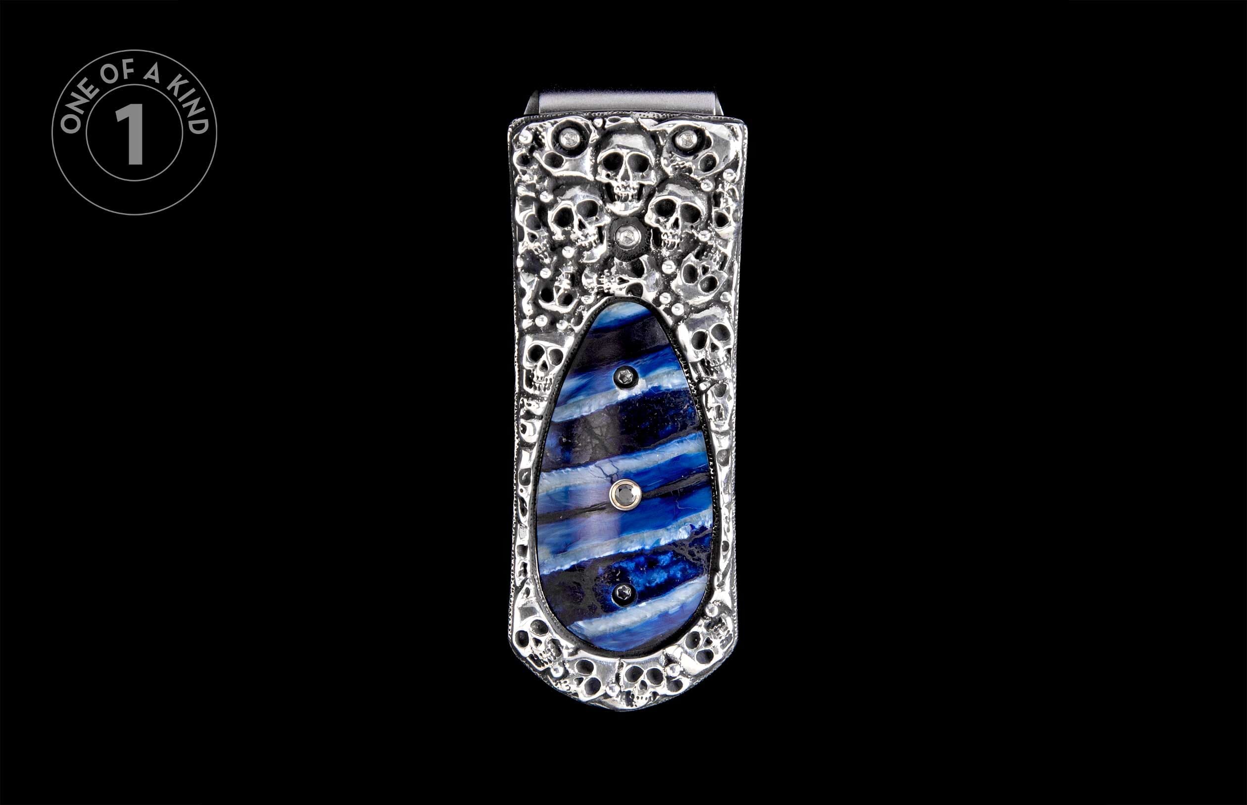 Silver-toned money clip with embossed skull design and a blue striped resin inlay accented with small crystals.