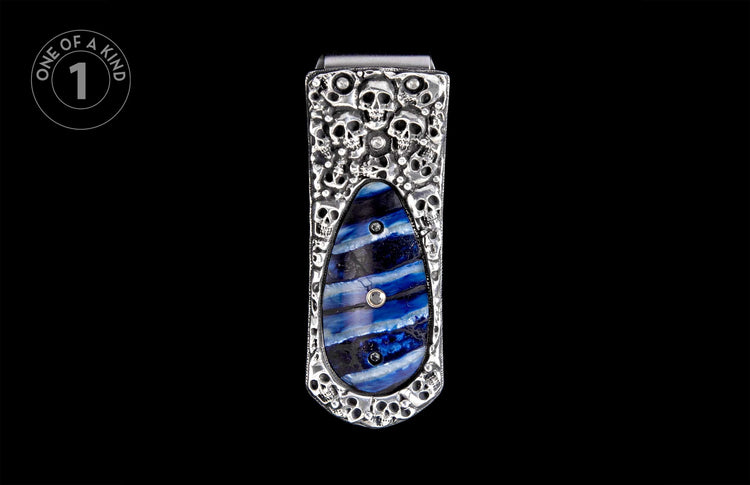 Silver-toned money clip with embossed skull design and a blue striped resin inlay accented with small crystals.