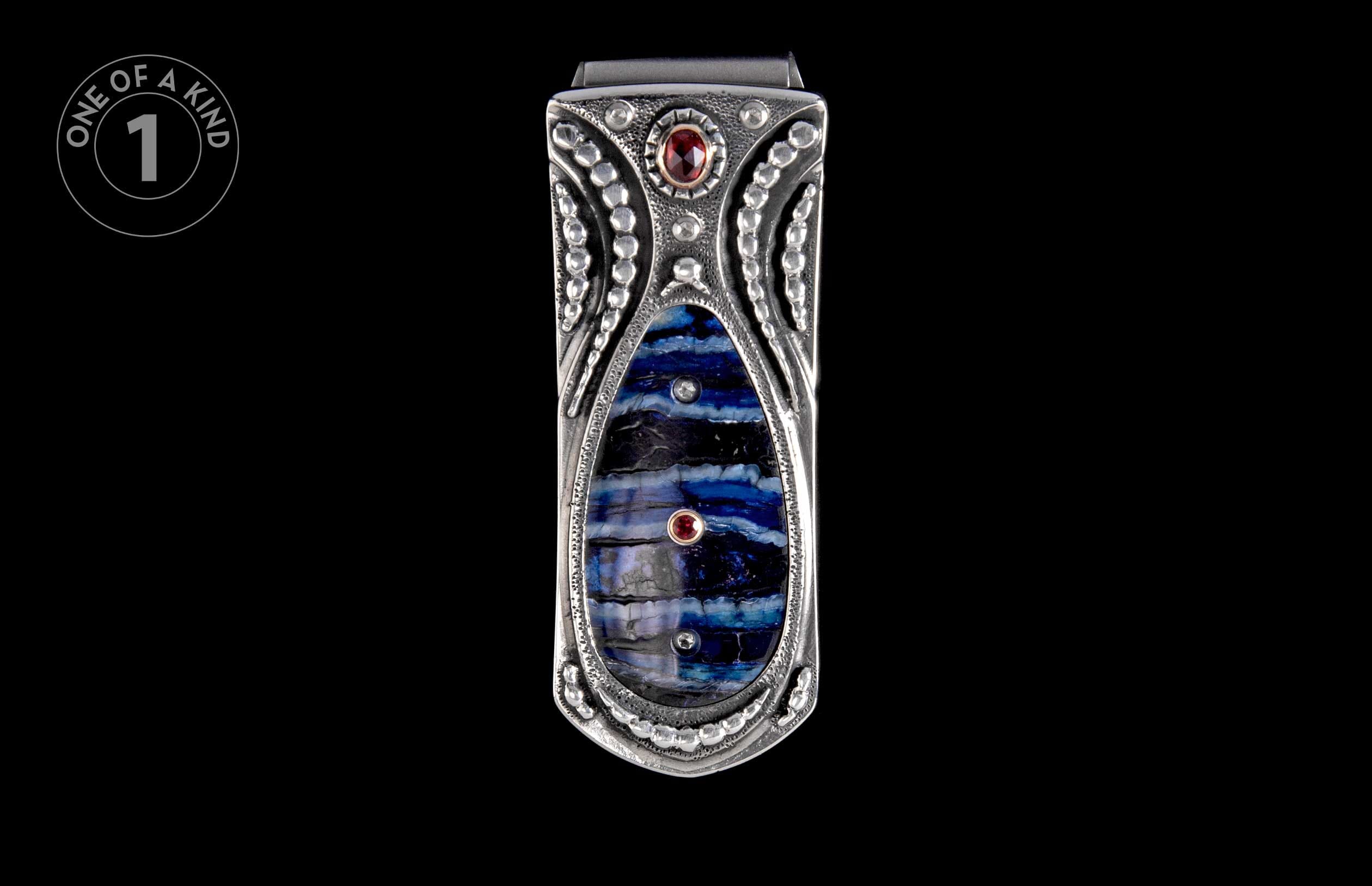 Silver money clip with intricate design, featuring a striped blue and black stone inlay and two small red gemstones.