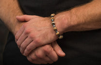 Beaded bracelet featuring textured beige beads and smooth silver spacers worn on a man's hairy wrist.
