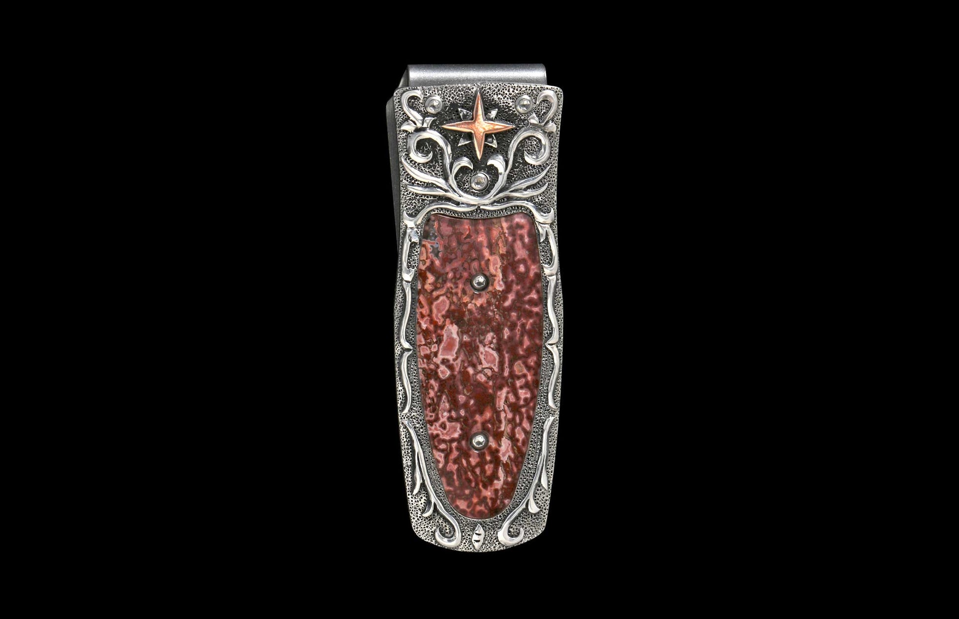 Silver money clip with an ornate textured frame, featuring a reddish-brown patterned stone inlay, a copper-toned star, and scroll details.