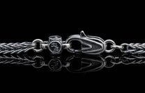 Silver braided chain with an ornate lobster clasp and 'HM' engraved barrel connector on a reflective surface.