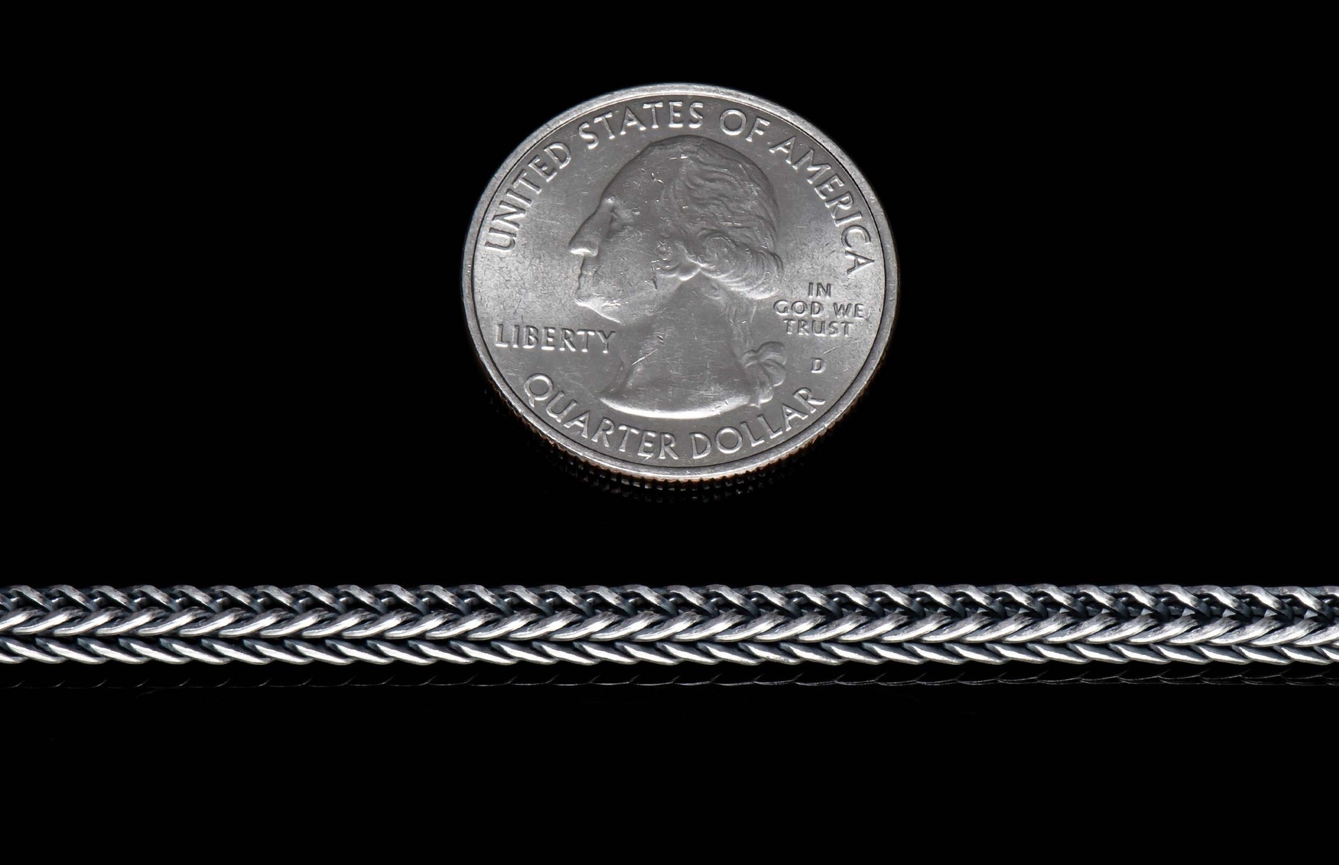 Silver jewelry chain with intricate braided links, shown horizontally with a US quarter dollar coin for scale.