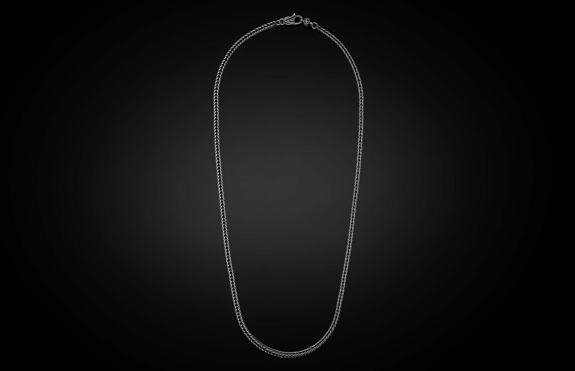 Silver-toned woven chain necklace with a detailed lobster clasp, laid flat.