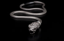 Silver snake-shaped jewelry with a braided body and detailed head with open jaws, on a black background.