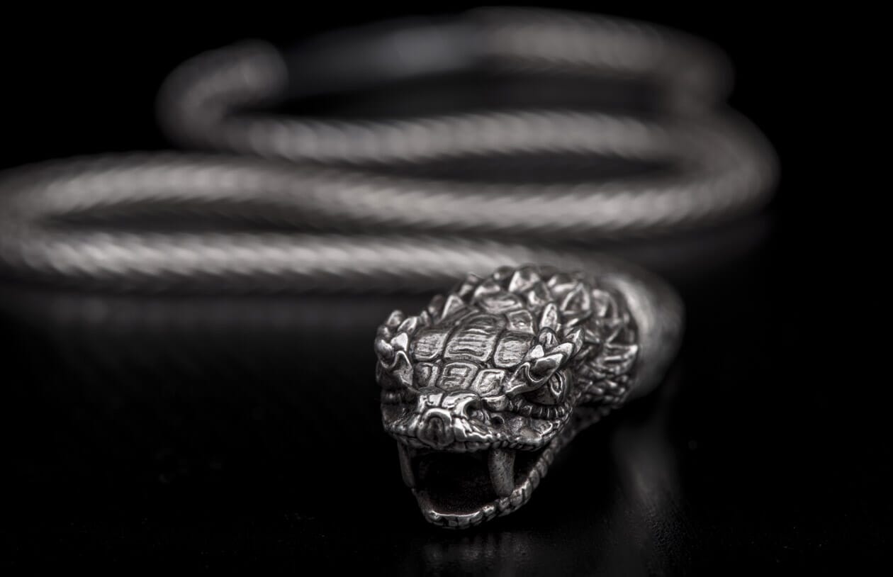 Silver-toned snake head bracelet with detailed scales, open mouth, fangs, and braided coiled body.