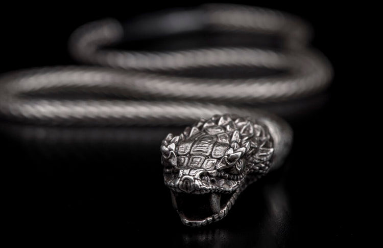 Silver-toned snake head bracelet with detailed scales, open mouth, fangs, and braided coiled body.