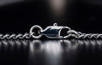 Silver chain necklace with a polished lobster clasp and textured links, viewed close-up on a dark reflective surface.