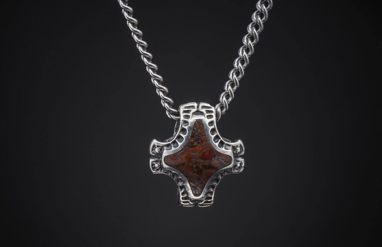 Silver pendant with a mottled reddish-brown stone in an ornate openwork frame, on a twisted chain.