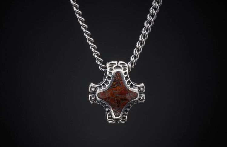 Silver pendant with a mottled reddish-brown stone in an ornate openwork frame, on a twisted chain.